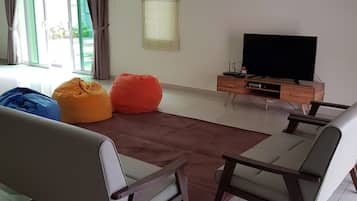 A living room with a sofa, two bean bags, a coffee table, a TV on a wooden stand, and a sliding glass door.