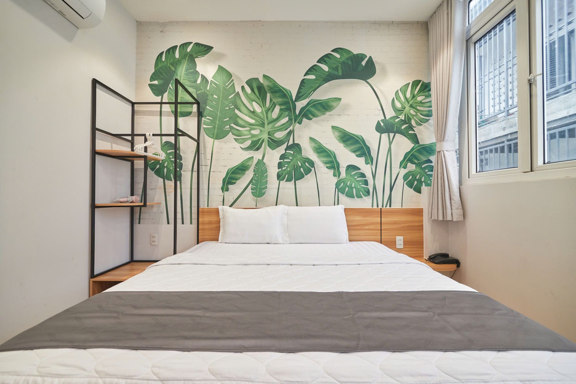 Ein Schlafzimmer mit einem Bett, einem Nachttisch, einer Regaleinheit und einer großen Wandmalerei mit grünen Blättern.