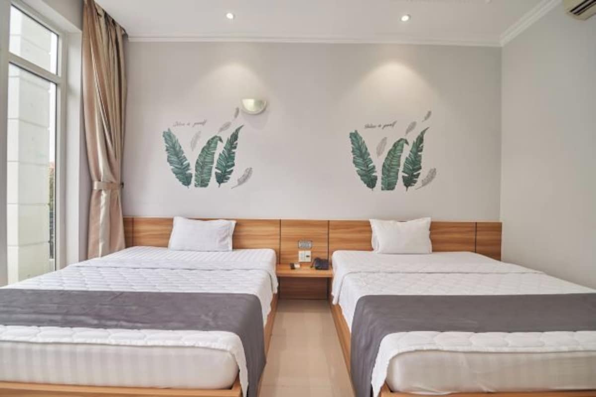 Habitación de hotel con dos camas, cabecera de madera, mesita de noche con teléfono y lámpara, y una pared decorada con motivos de hojas.