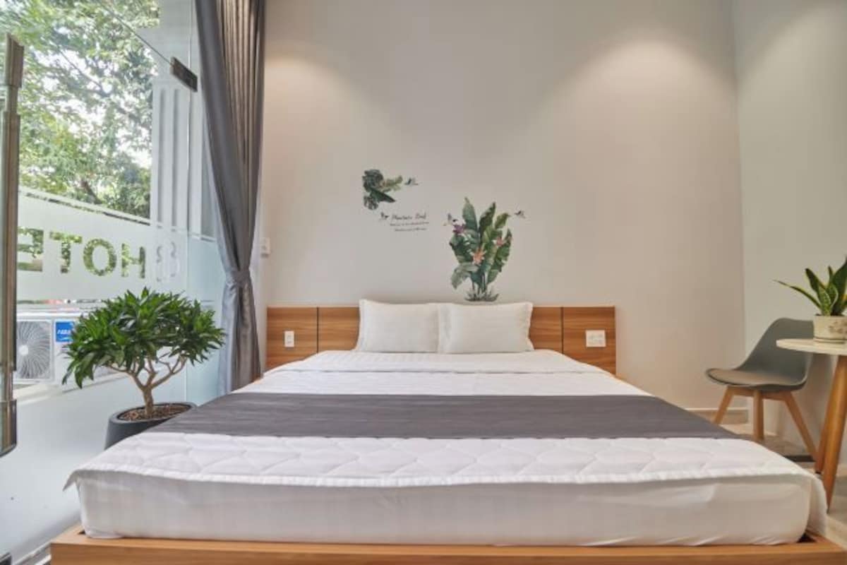 Una cama bien hecha con cabecera de madera, una pequeña planta en maceta y una obra de arte colgada en la pared.