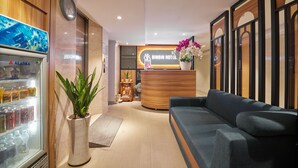 A hotel reception area with a reception desk, a clock, a refrigerator stocked with beverages, a potted plant, and a sofa. - Bin Bin Hotel 2 - Near Him Lam D7 (Ho Chi Minh City)