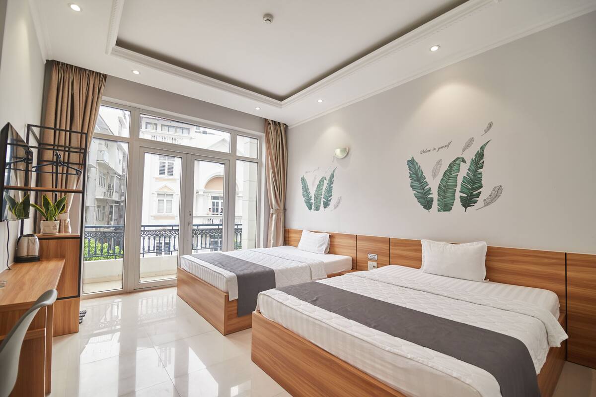 Une chambre d’hôtel avec deux lits, un bureau et un balcon donnant sur des immeubles.