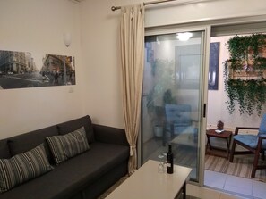 Uma sala de estar com um sofá escuro, uma porta de vidro que dá para uma varanda, e uma mesa com uma garrafa e copos.