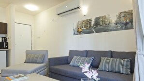 A modern living room with a grey sofa, striped pillows, a coffee machine, and a framed cityscape picture on the wall. - TLV Suites By The Sea - 2 Rooms (Tel Aviv)