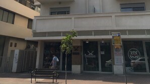 A multi-story building with balconies, a storefront with a sign, and a pedestrian walkway. - TLV Suites By The Sea - 2 Rooms (Tel Aviv)