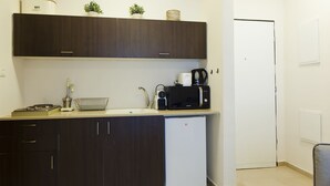 A compact kitchen with dark wood cabinets, a white refrigerator, a microwave, a coffee maker, and a sink. - TLV Suites By The Sea - 2 Rooms (Tel Aviv)