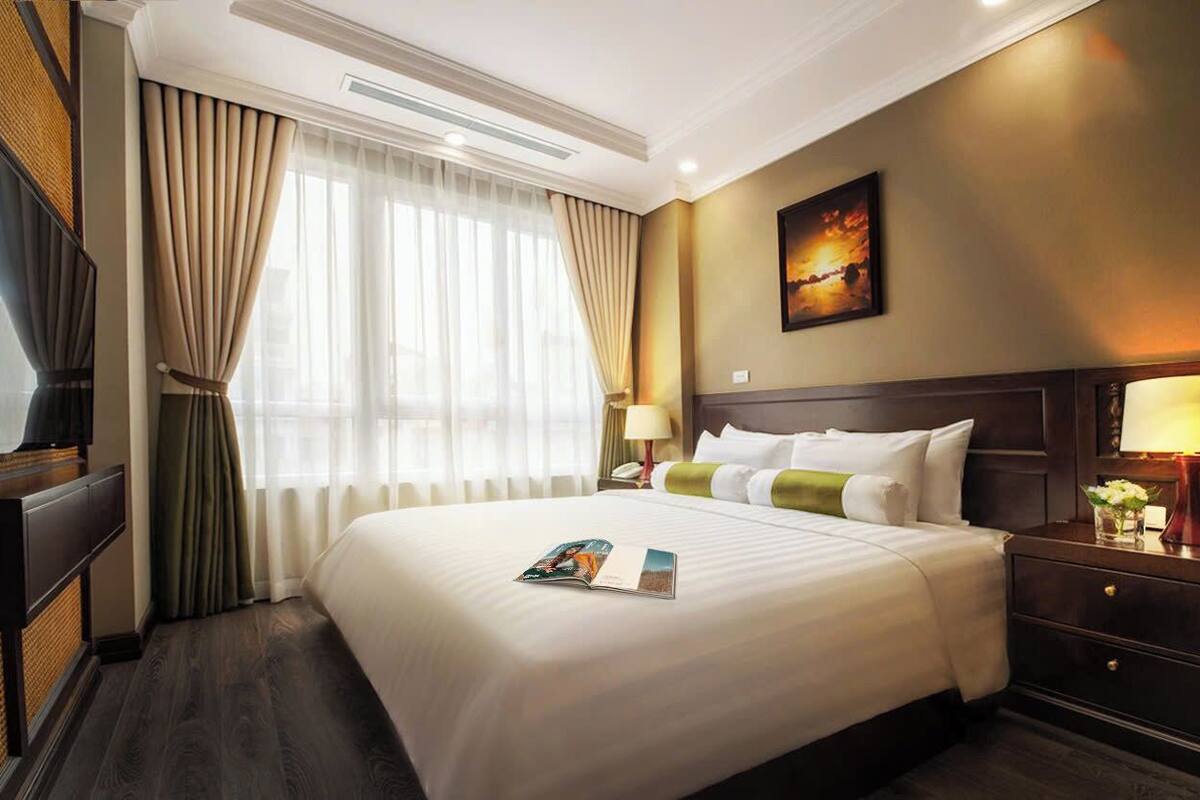 A hotel room with a large bed, a television, a nightstand with a lamp, and a painting on the wall.
