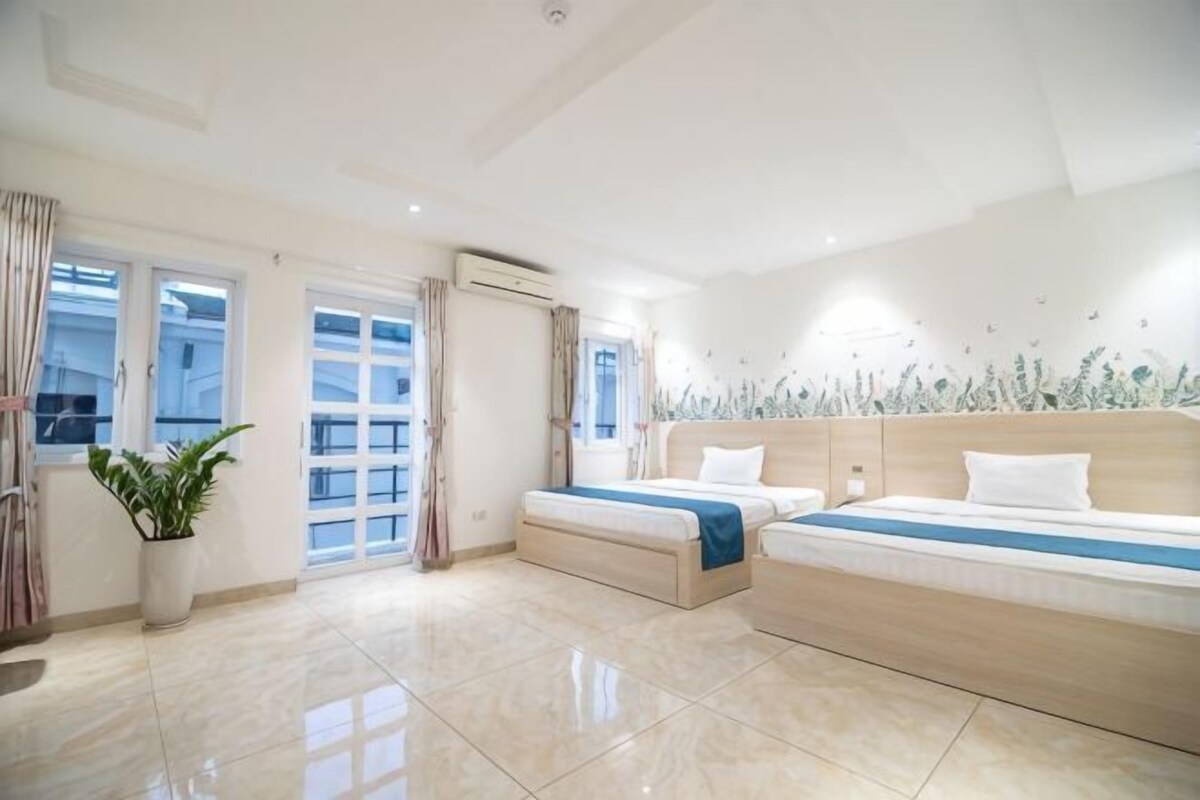 Una camera d'albergo moderna con un letto grande, un letto più piccolo, una pianta in vaso e un balcone con tende.