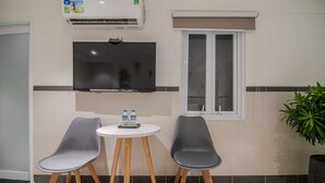 A small room with two grey chairs, a white table with water bottles, a flat-screen TV, and a window with blinds. - BinBin Hotel 5 - Near Lotte Mart D7 (Ho Chi Minh City)