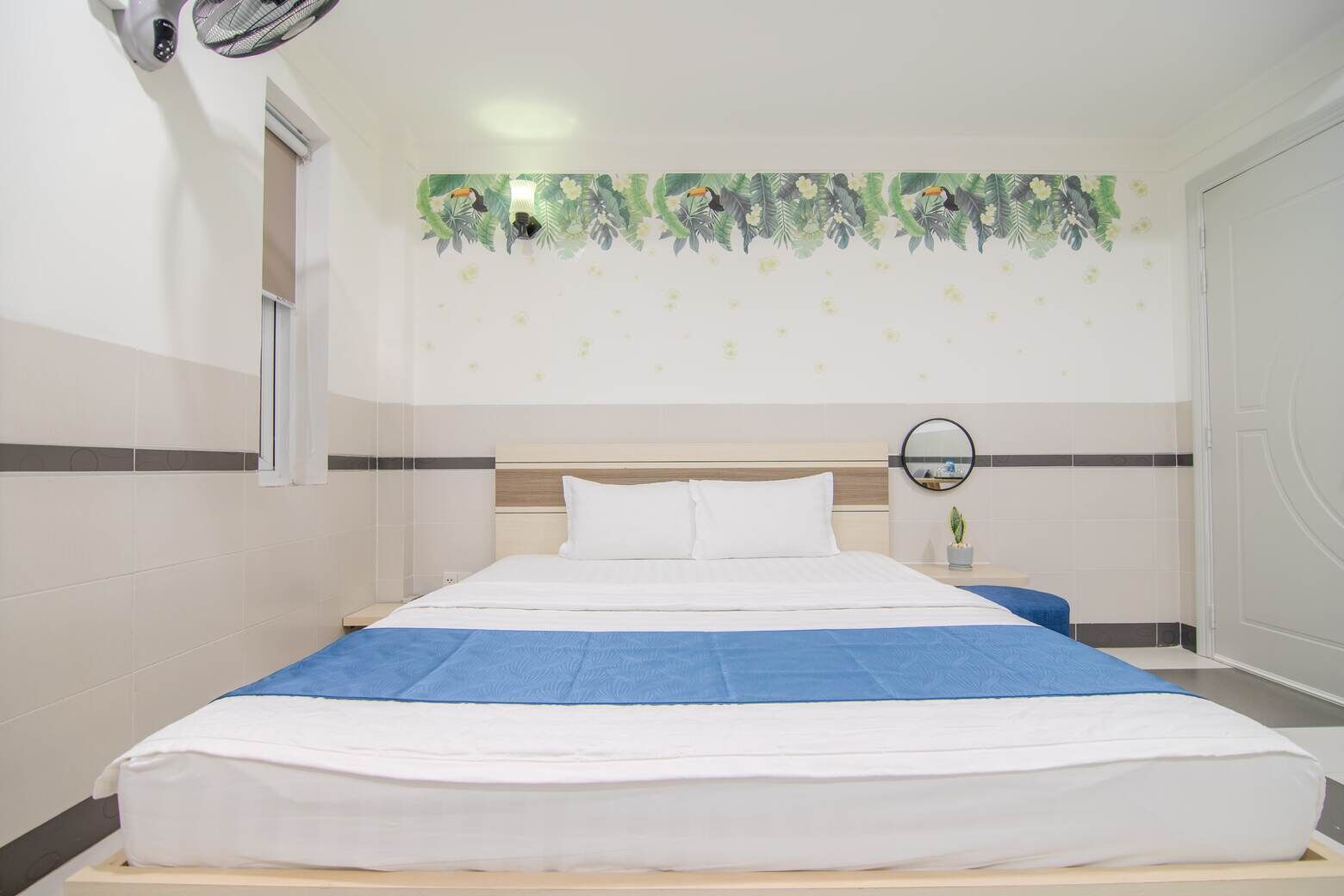 Habitación de hotel con una cama grande, una mesita de noche pequeña con un espejo y una pared con un borde de motivos tropicales.