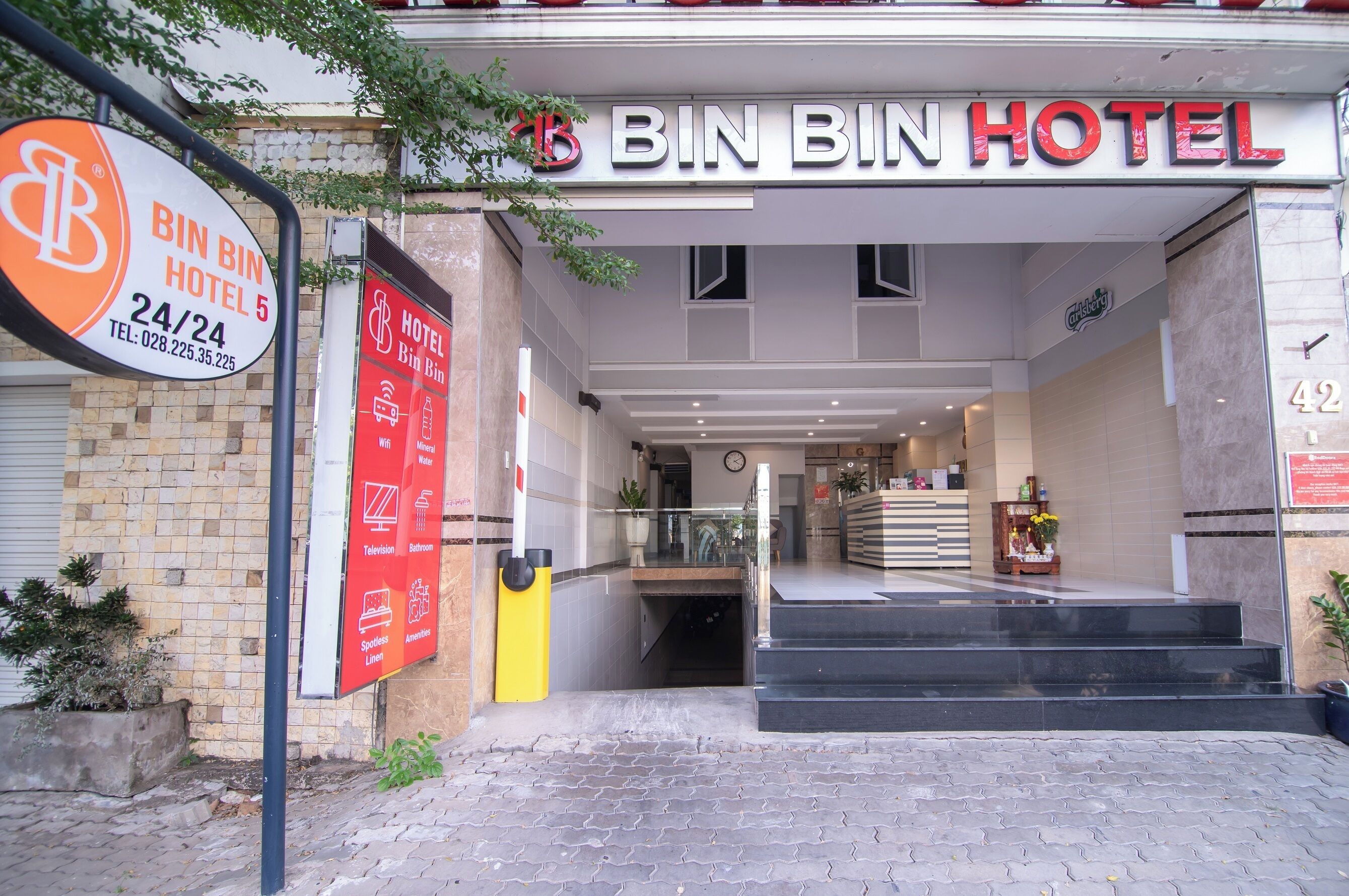 The entrance to Bin Bin Hotel with a clear sign, a staircase leading inside, and a reception area visible through the glass doors.