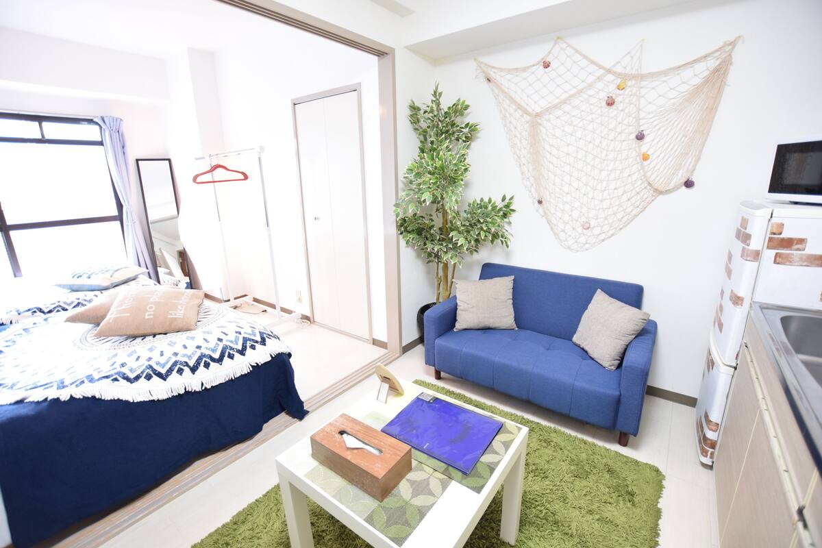A bedroom with a bed, a blue sofa, a small table, and a green rug.