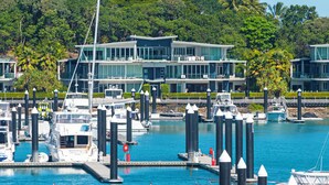A marina with boats docked, a modern building with balconies, and a clear blue waterfront.