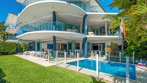 A modern multi-story house with a swimming pool, glass railings, and outdoor seating.