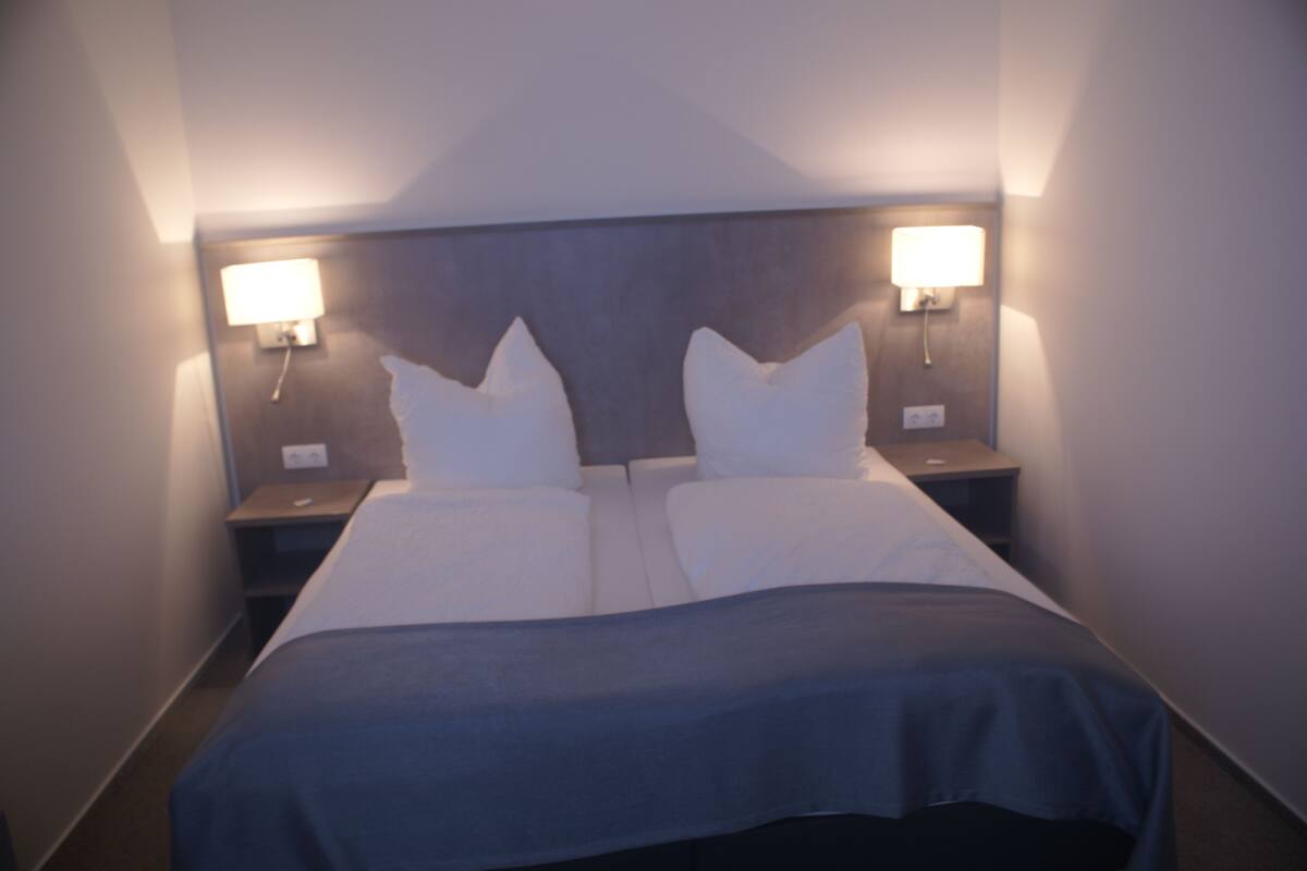 A hotel room with a double bed, two bedside tables, and two wall-mounted lamps.