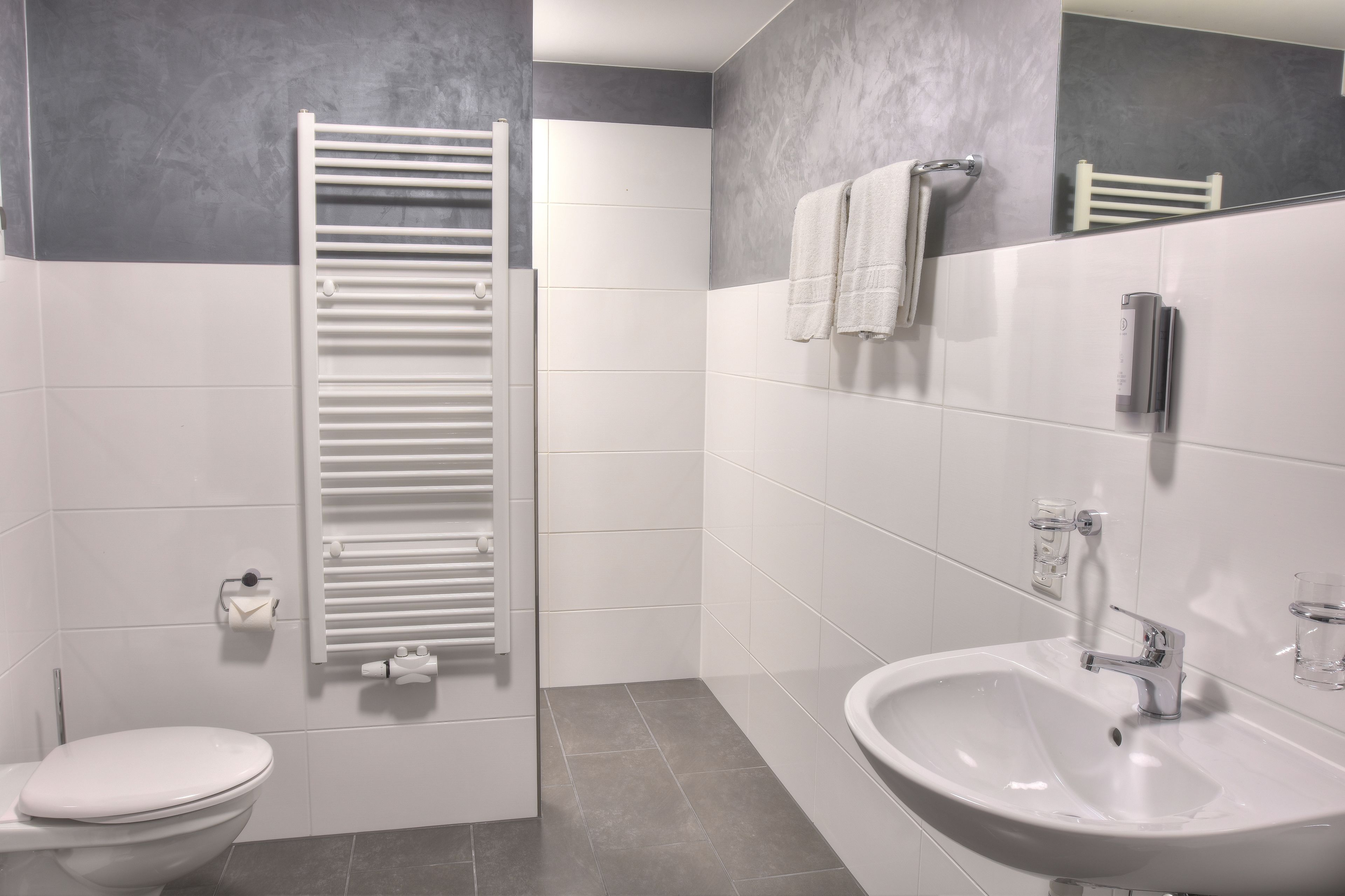Un baño moderno con inodoro, un lavamanos blanco, un toallero y una toalla colgada en la pared.