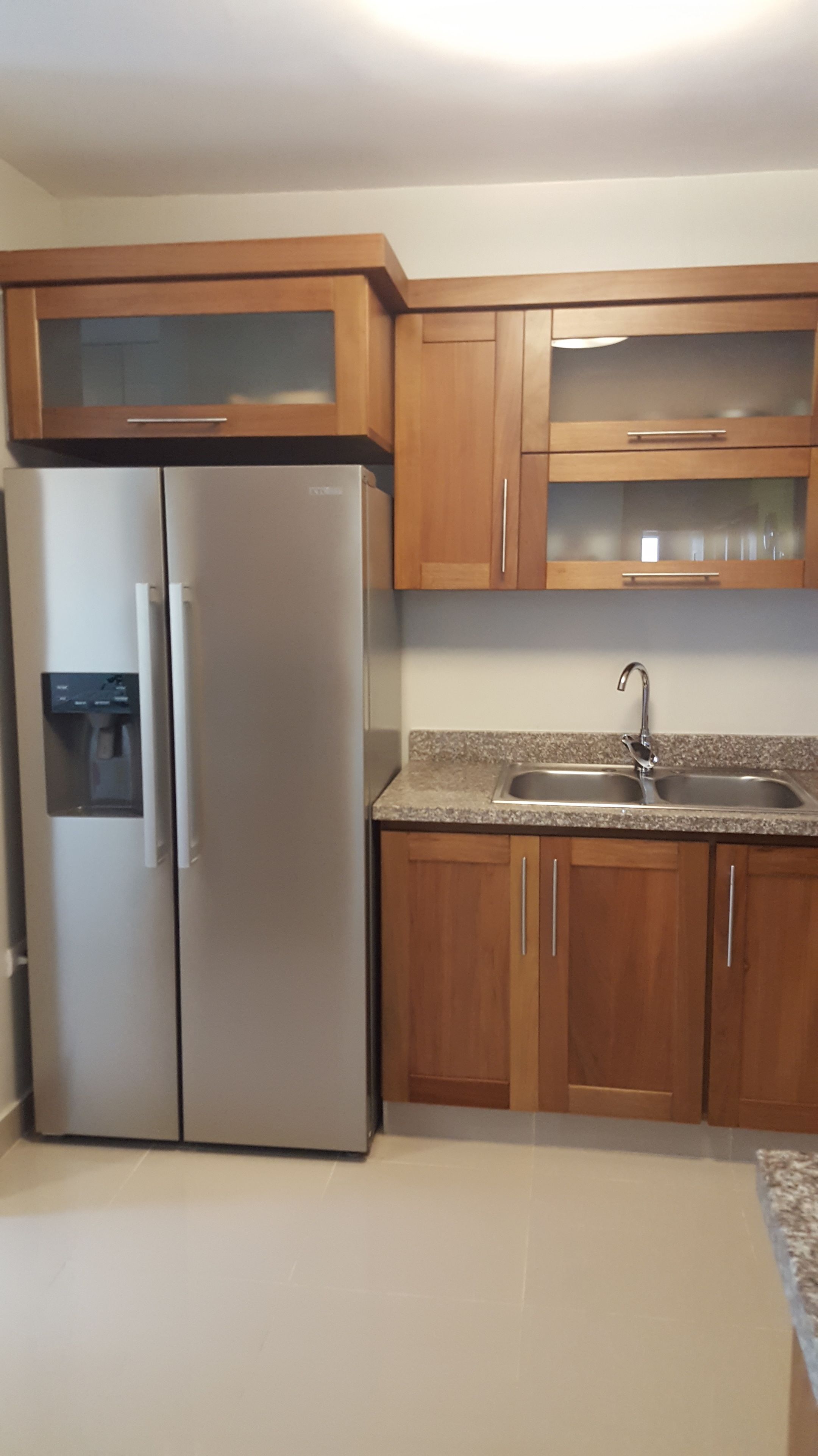 A kitchen with a stainless steel refrigerator, wooden cabinets, a granite countertop, and a stainless steel sink.
