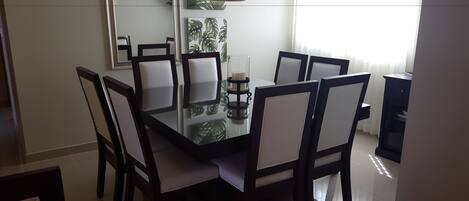 Un comedor con una mesa de vidrio rodeada de sillas, un centro de mesa con velas y un espejo colgado en la pared.
