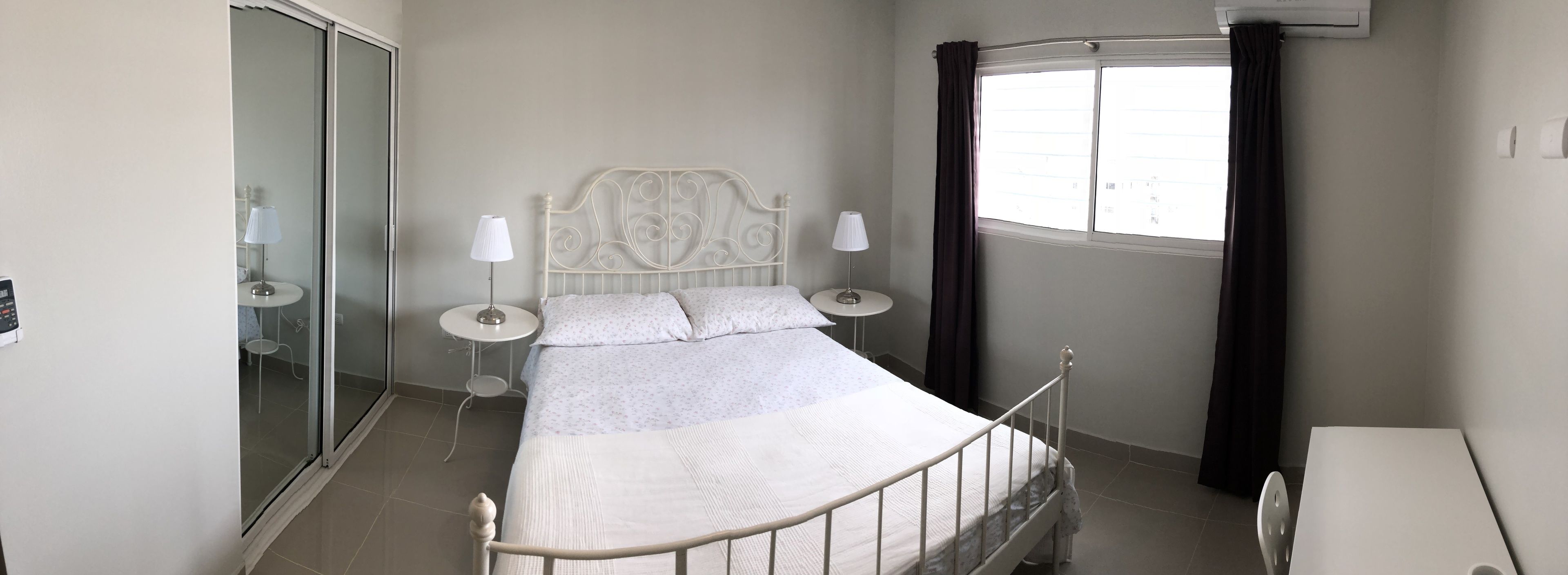A bedroom with a bed, two bedside tables, a window with curtains, and a sliding door.
