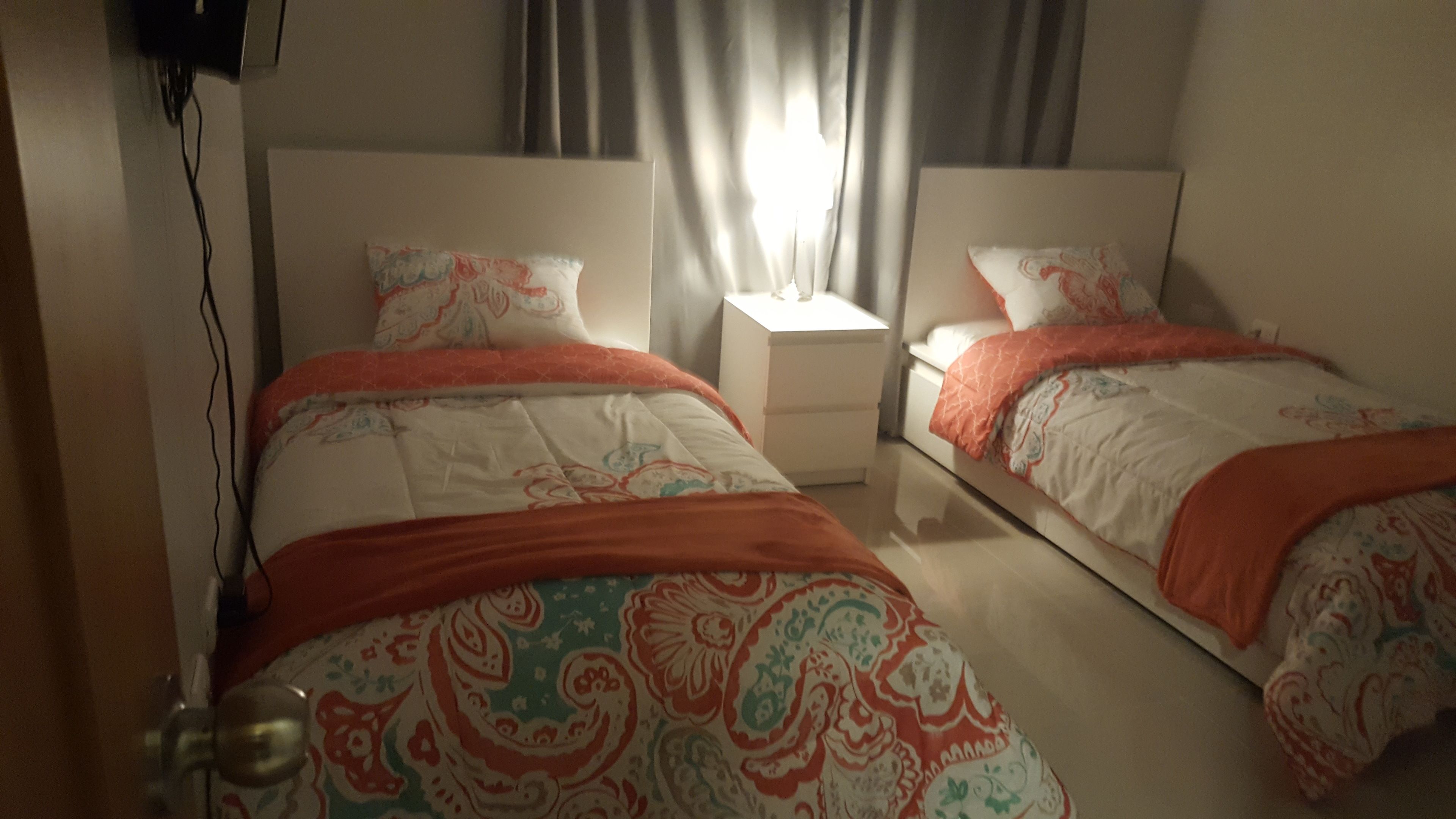 Ein Schlafzimmer mit zwei Betten, beide mit gemusterten Bettdecken und passenden Kissen. Ein Nachttisch mit Lampe befindet sich zwischen den Betten.