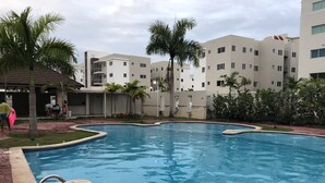 A swimming pool surrounded by palm trees and a building with multiple balconies. - HeimatDorado R.D. your pleasant stay (Santiago de los Caballeros)