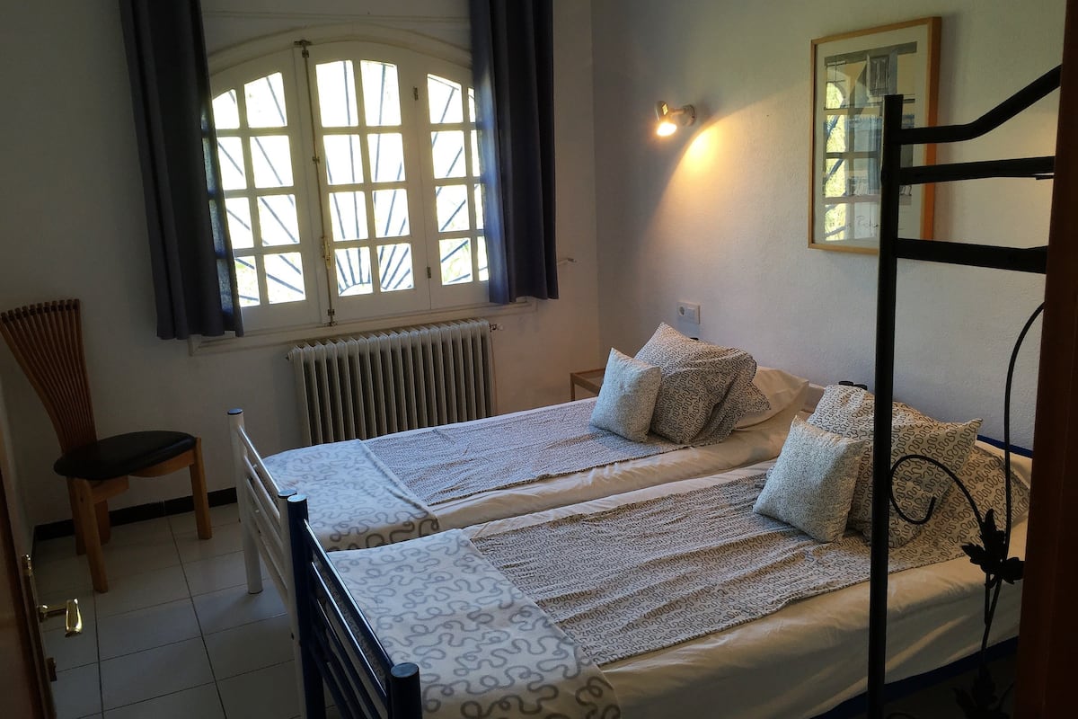 Quarto com duas camas, um radiador, uma cadeira e uma janela com cortinas.