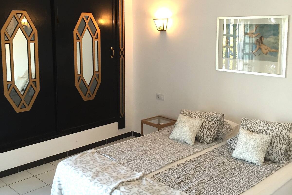 Quarto com cama, guarda-roupa, luz acoplada à parede e quadro emoldurado.