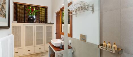 A modern bathroom with a glass shower enclosure, a wooden vanity, a sink, and a mirror.
