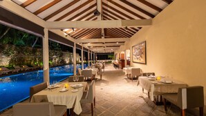 A restaurant with tables set for dining, a pool area, and a view of the outdoors.