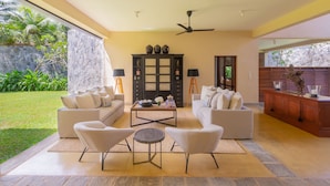 A spacious living room with a large window, a ceiling fan, and a stone wall.