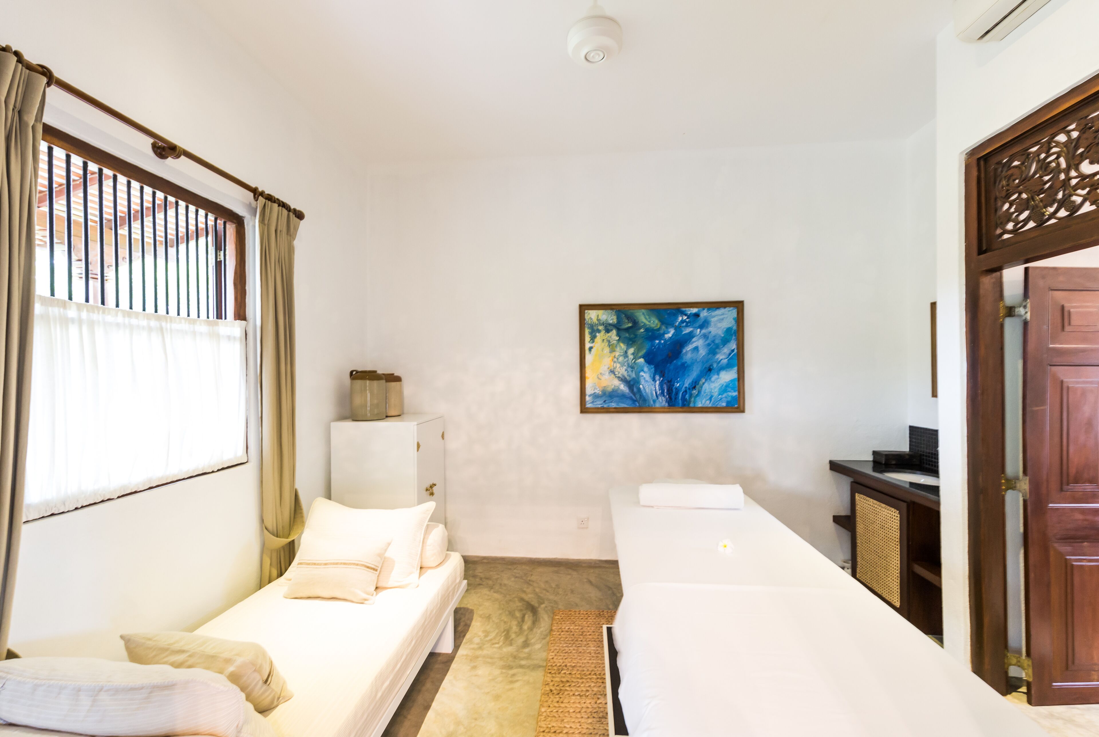 A room with two beds, a painting on the wall, and a wooden door.