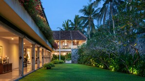 A two-story building with a balcony, surrounded by lush greenery and palm trees.