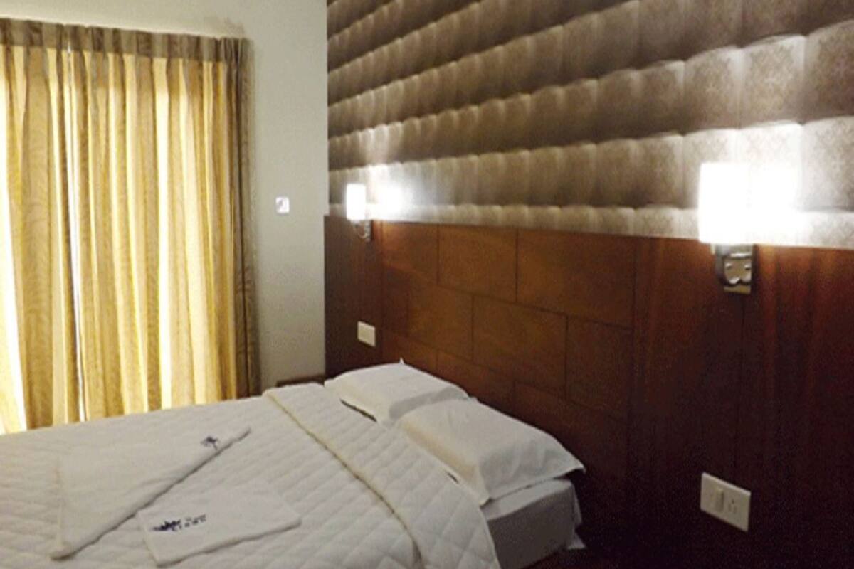 Una habitación de hotel con cama, cortinas y cabecera con iluminación integrada.