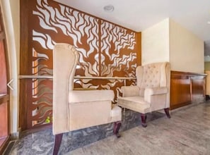 Un vestíbulo con un papel tapiz estampado, dos sillones tapizados y un mostrador de recepción de madera.