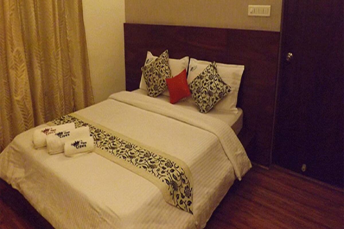 Una cama bien hecha con almohadones estampados, cabecera y suelo de madera.