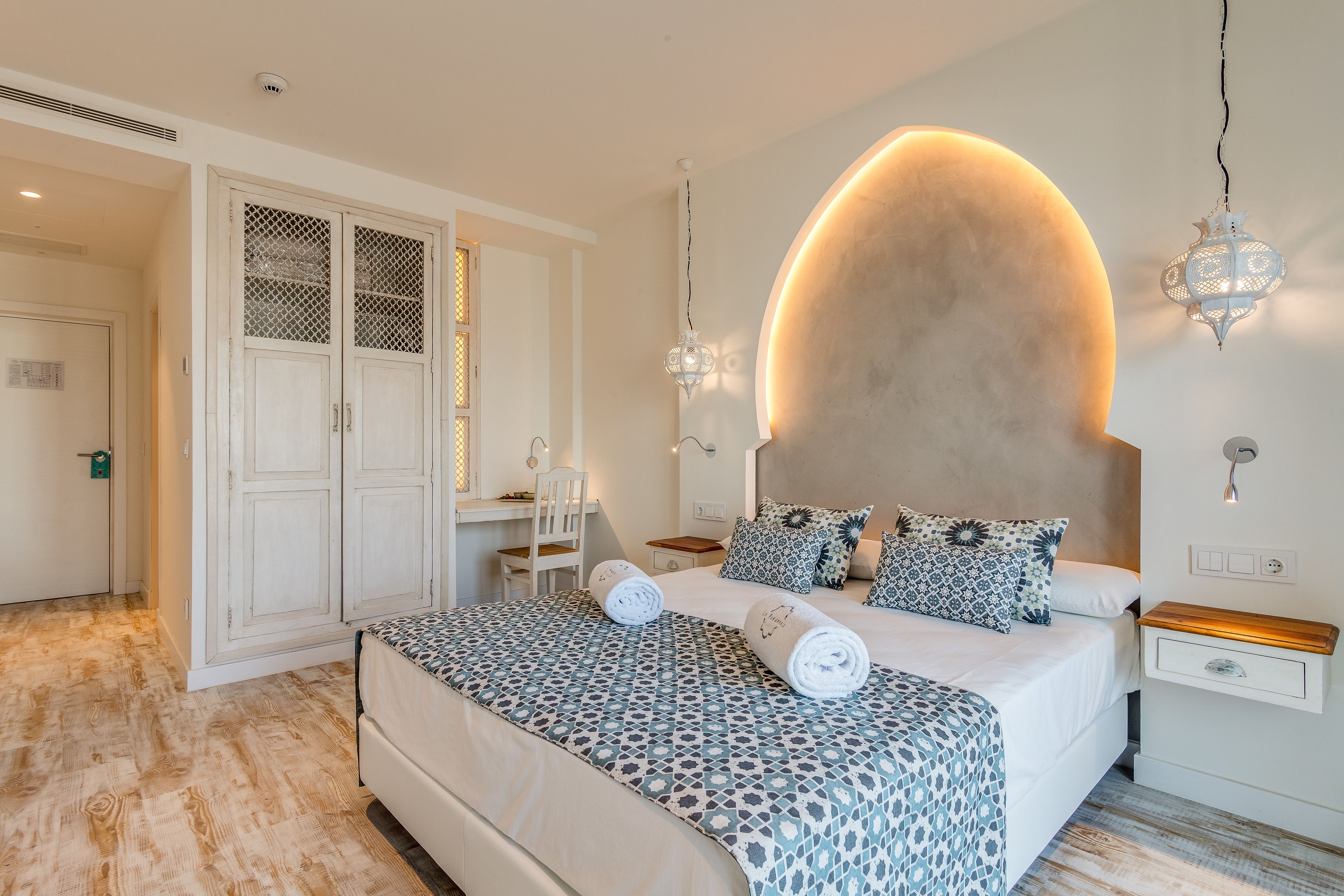 A bedroom with a large bed, a desk, and a wardrobe.