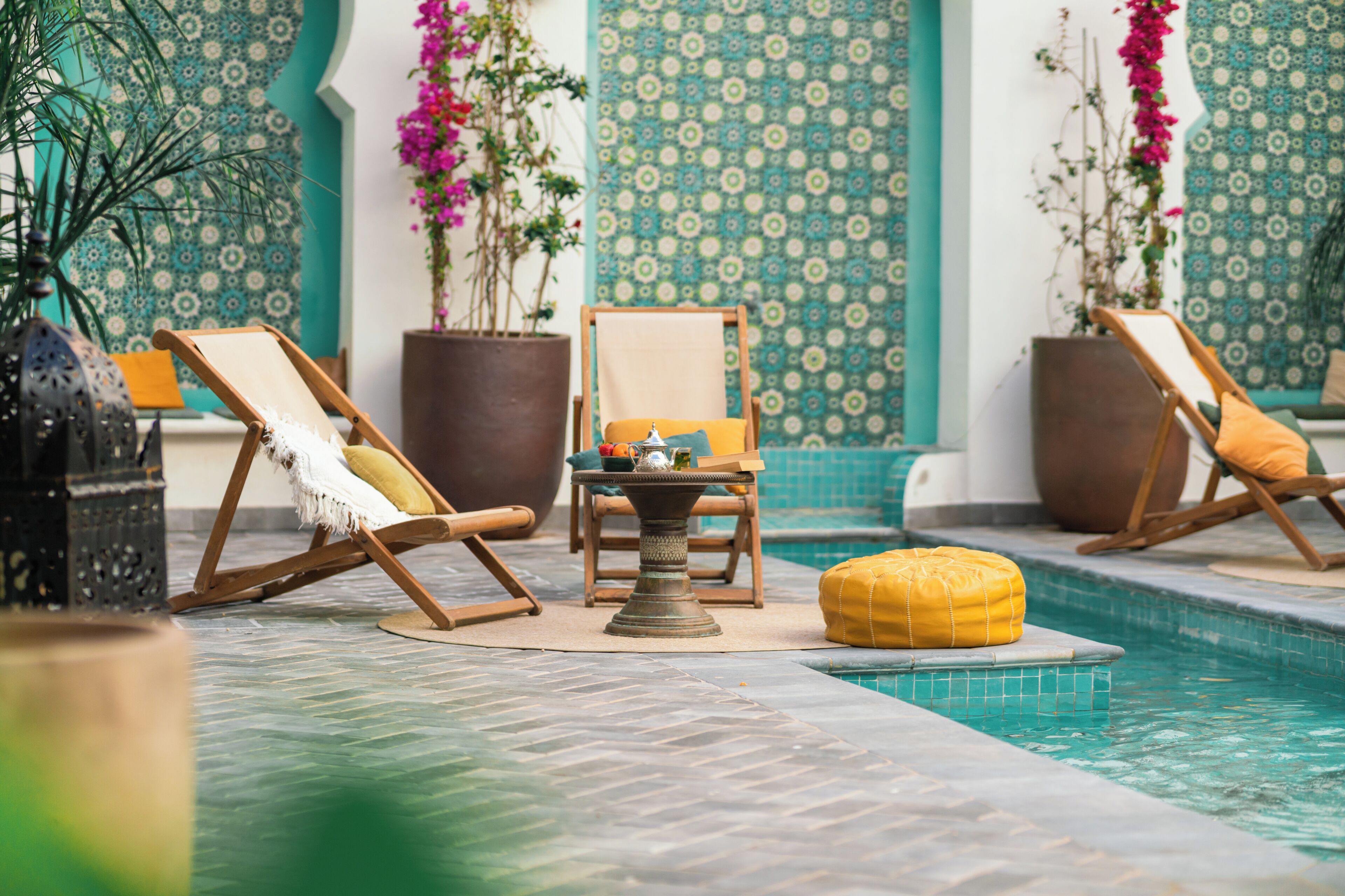 A poolside area with lounge chairs, a small table with a tray, and potted plants.