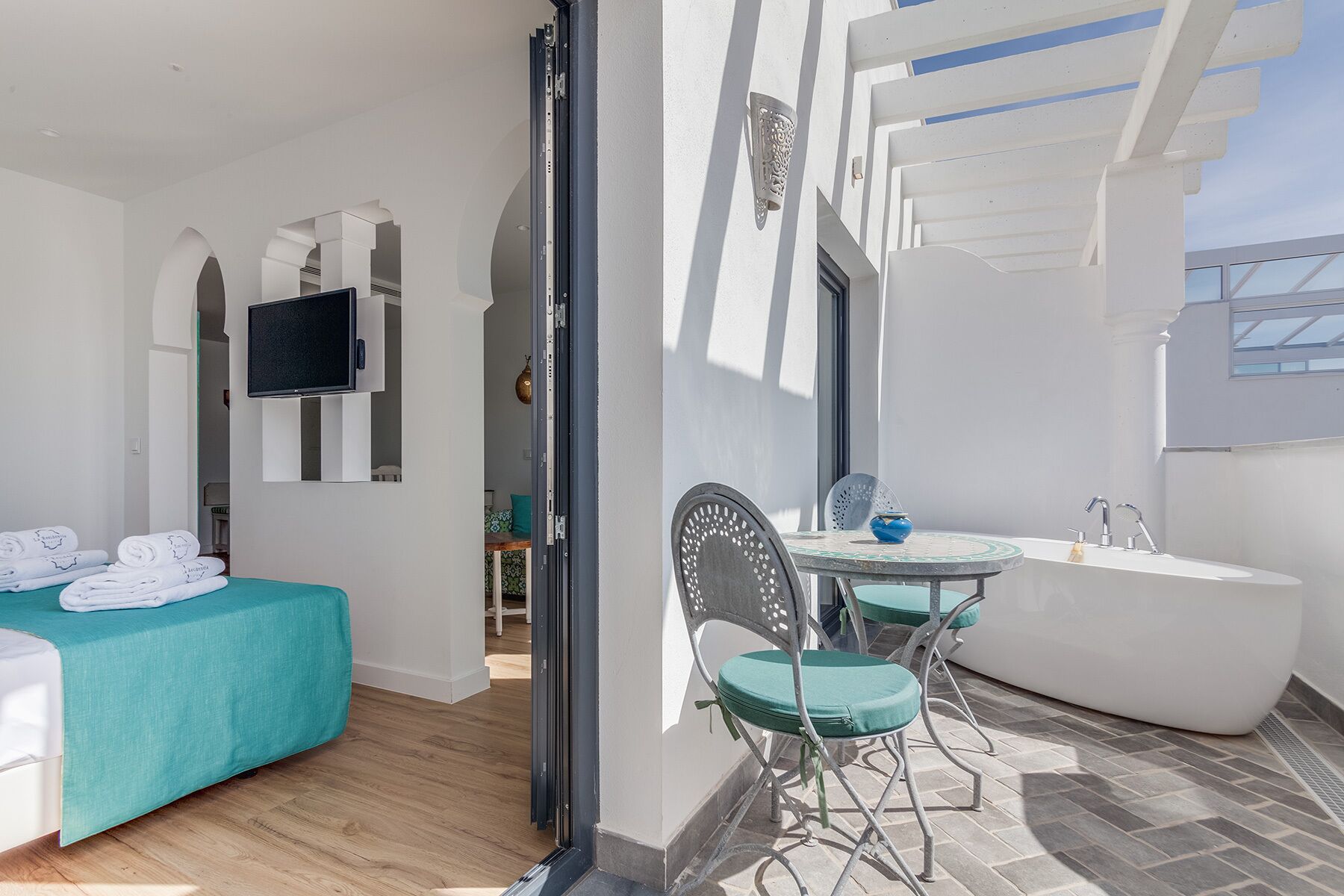 A modern hotel room with a bed, a desk, a chair, a bathtub, and a TV.