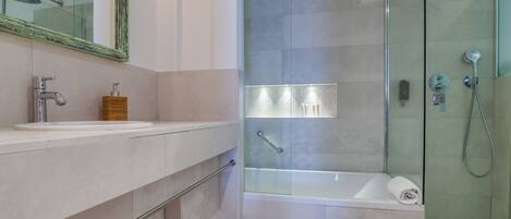 Une salle de bain moderne dotée d’une douche à parois de verre, d’une baignoire et d’un meuble-lavabo avec un miroir et un distributeur de savon.
