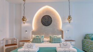 A modern hotel room with a unique arched ceiling, a bed with matching pillows, a nightstand, a chair, and a decorative wall piece. - Hotel & Spa La Residencia Puerto (Tarifa)