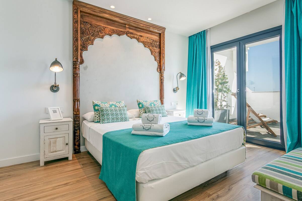 Quarto com cama grande, mesa de cabeceira, cômoda e vista para o exterior.