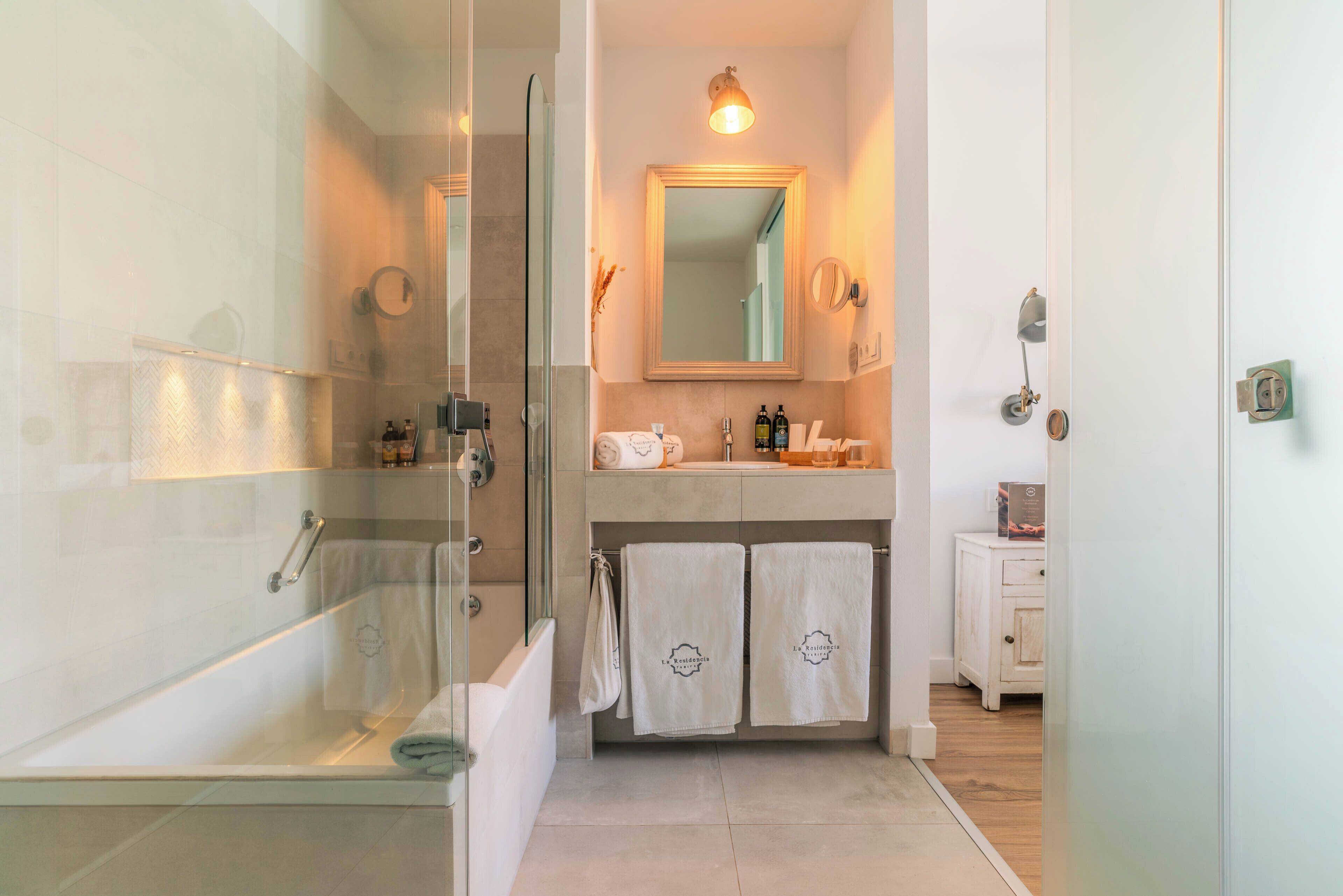 Une salle de bain avec une douche à parois de verre, un lavabo avec des articles de toilette et un miroir au-dessus.