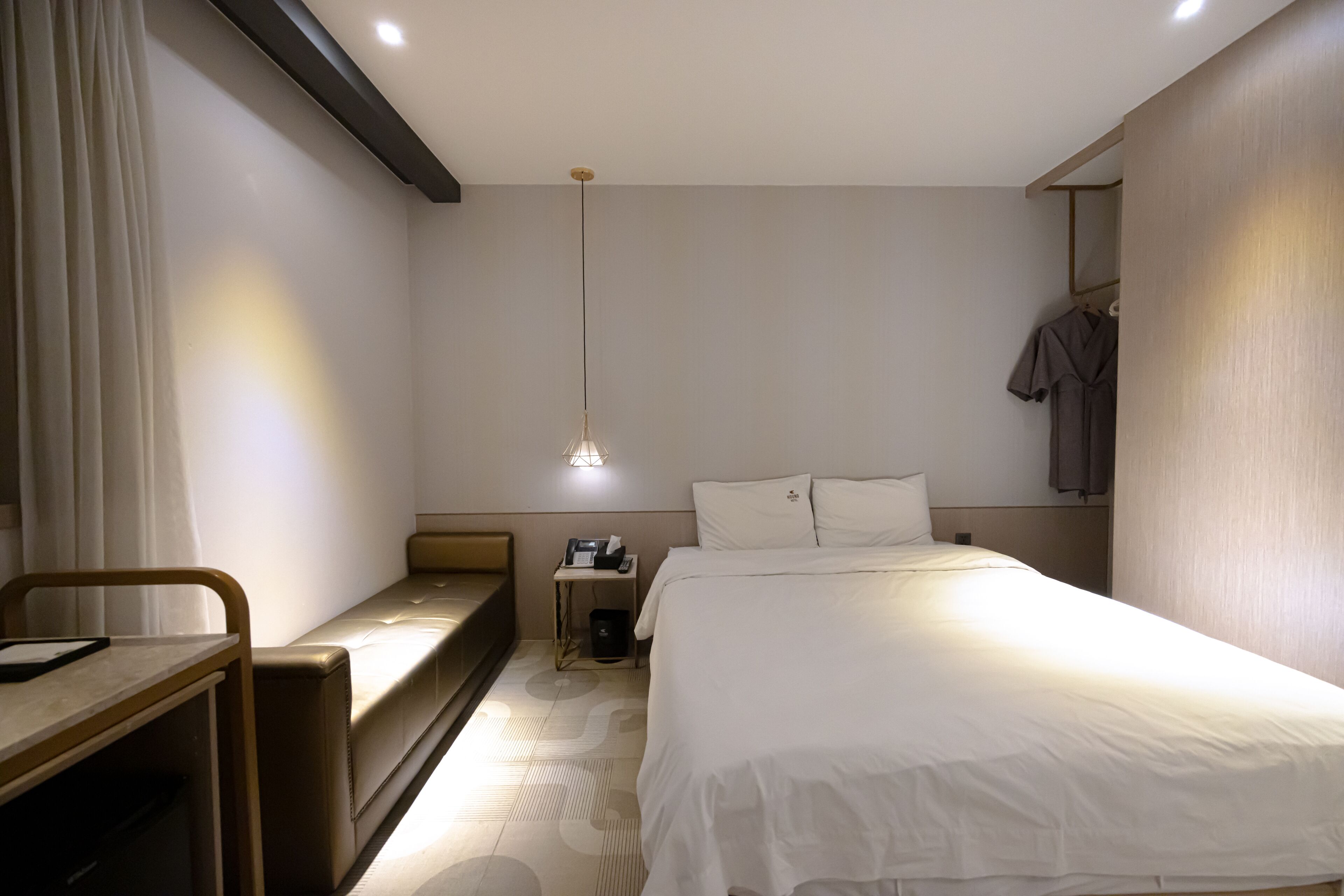 Ein Hotelzimmer mit Bett, Nachttisch, Lampe und einer Bank.