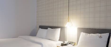 Habitación de hotel con dos camas, una mesita de noche, un teléfono y una pared con diseño de cuadrícula.