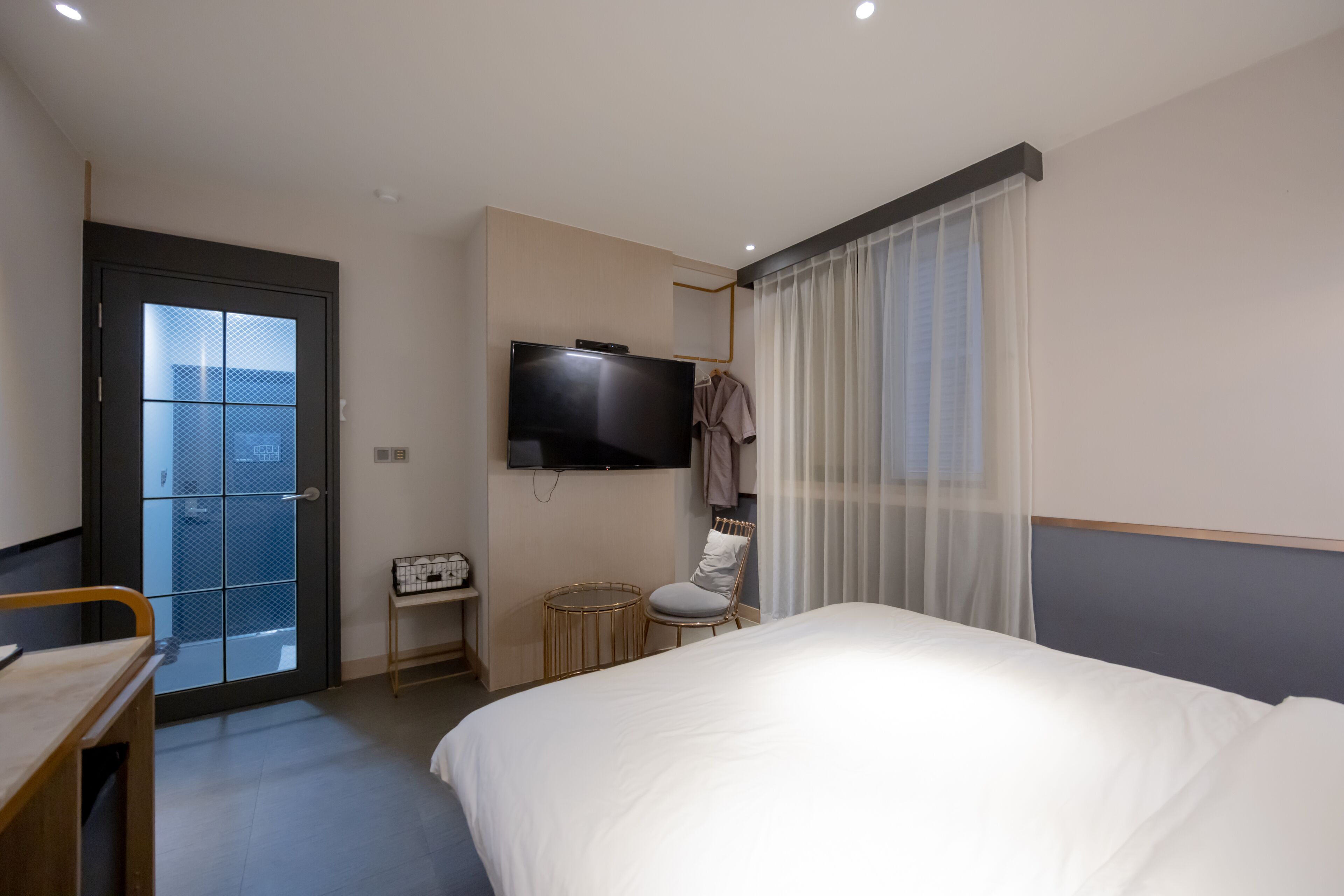 Una habitación de hotel con una cama, televisión, silla, mesita y una puerta que da a un balcón.