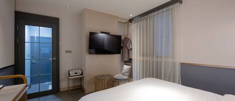 Una habitación de hotel con una cama, televisión, silla, mesita y una puerta que da a un balcón.