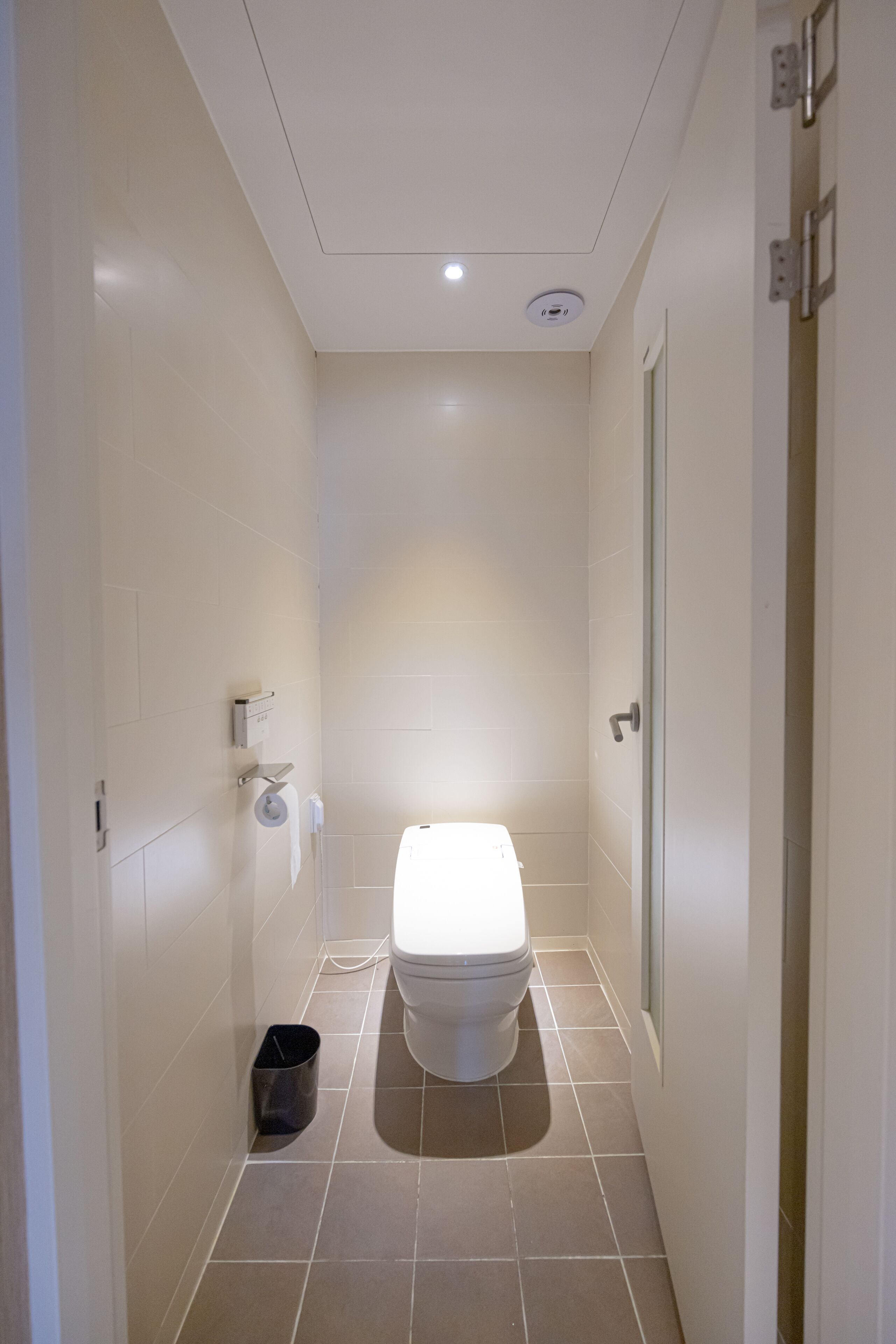 Un baño estrecho con un inodoro, un cesto de basura y un dispensador de papel higiénico en la pared.