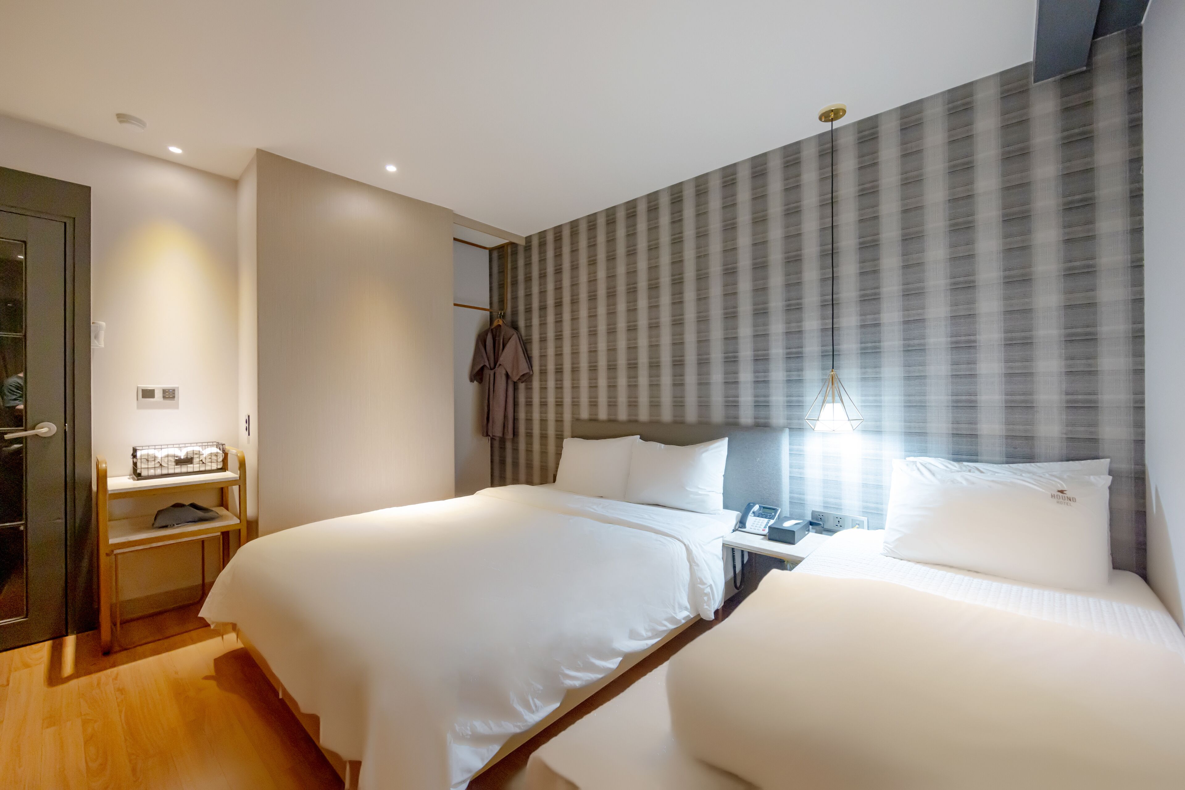 Habitación de hotel con dos camas, una mesita de noche con lámpara, un perchero y una maleta en el suelo.