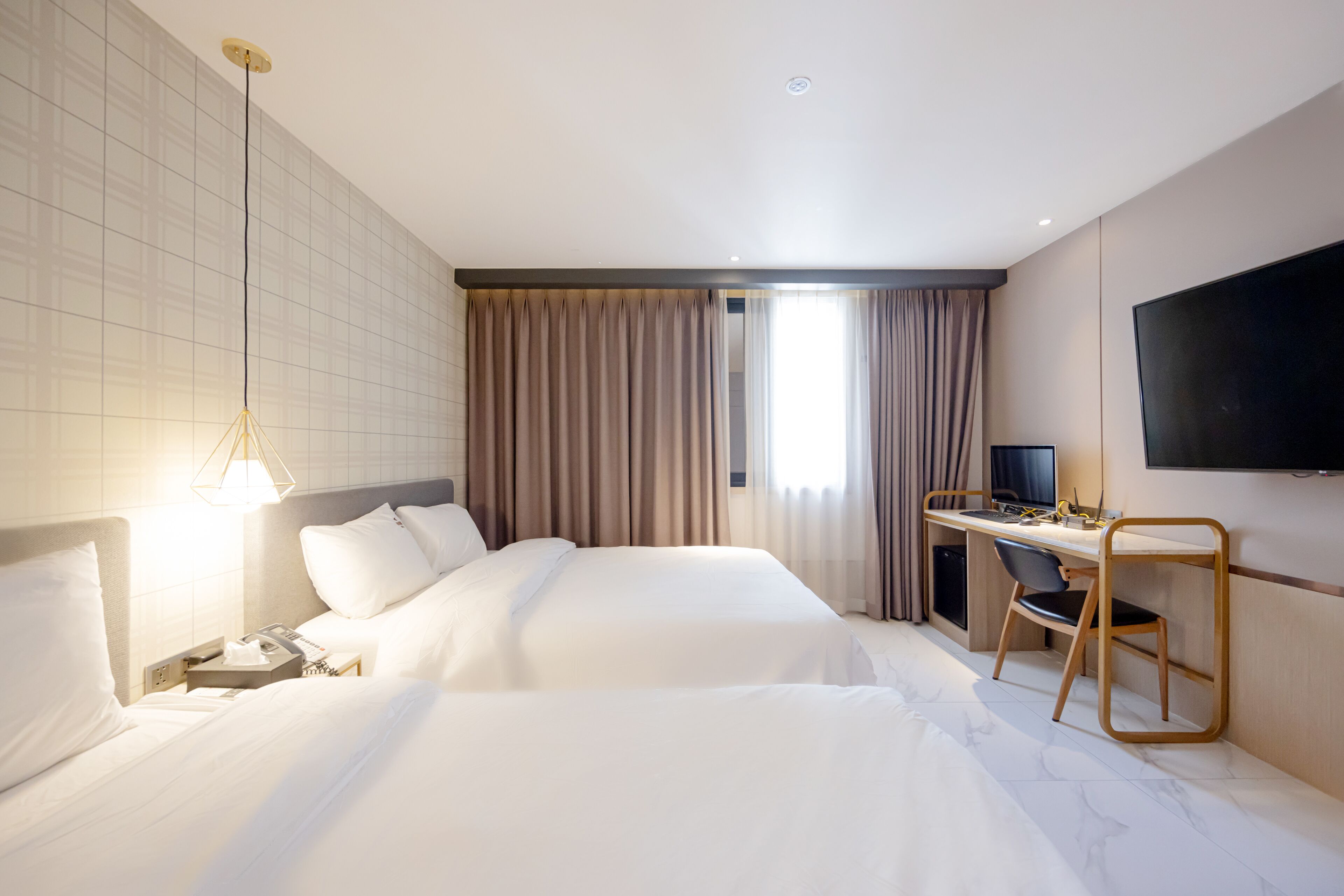 A hotel room with two beds, a desk, a chair, a TV, and a window with curtains.