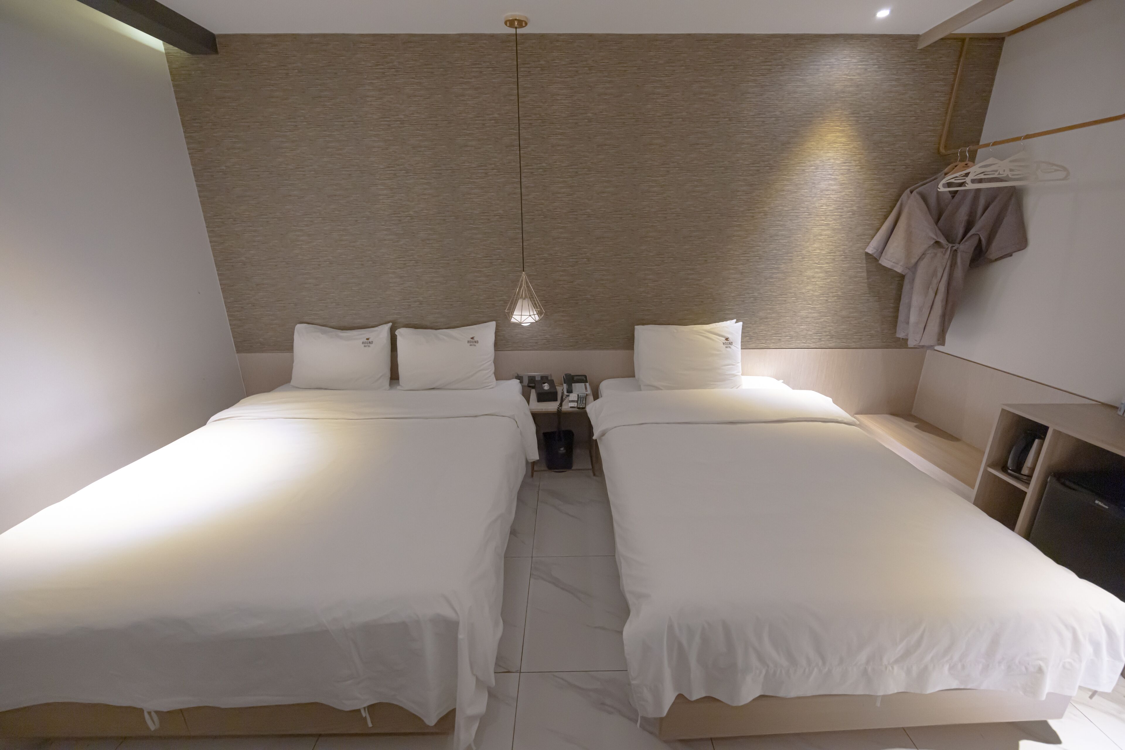 A hotel room with two single beds, a nightstand, a lamp, and a robe hanging on the wall.